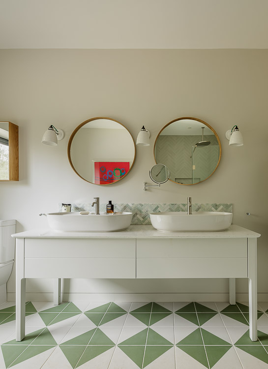 Contemporary duravit vanity unit with round wooden mirrors and green and white tiles
